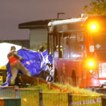 Emergency services at the scene of a fatal collision between a car and a bus on Bedfont Road in Feltham at night, with vehicles damaged and emergency lights flashing.