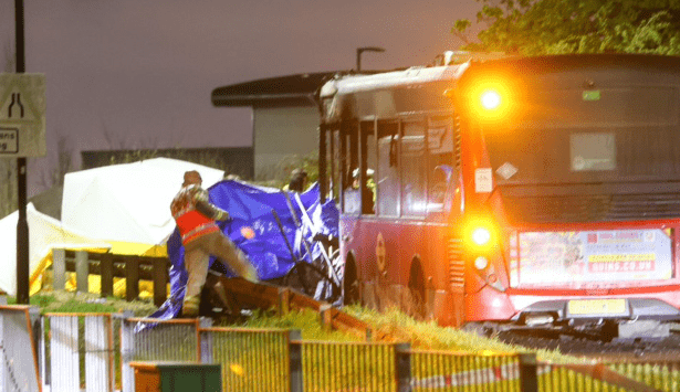 Emergency services at the scene of a fatal collision between a car and a bus on Bedfont Road in Feltham at night, with vehicles damaged and emergency lights flashing.